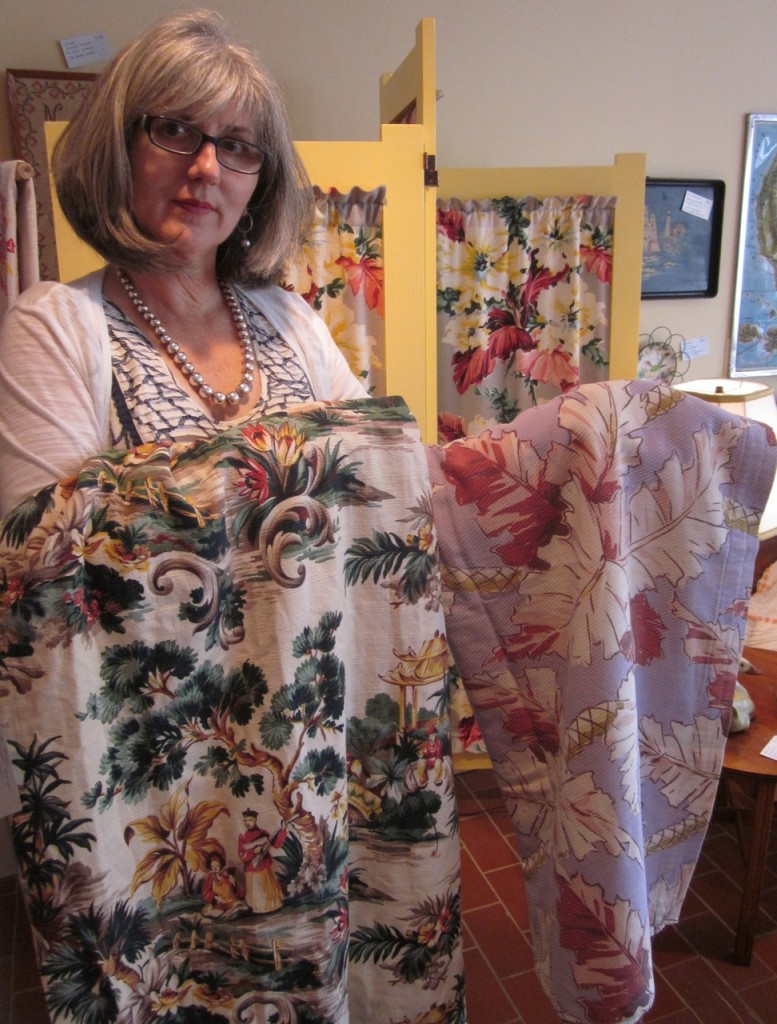 Holding up some vintage barkcloth pieces in front of a three-panelled screen with vintage barkcloth as well.