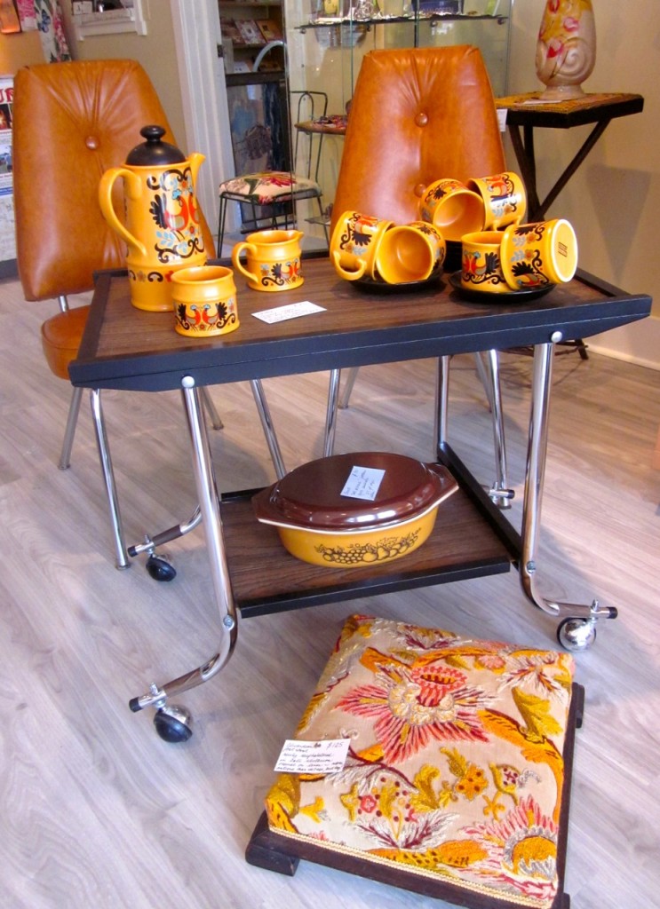 Antique chenille covered foot stool $125 Old Orchard Pyrex casserole $30 Sadler coffee set $75. Pair of orange vinyl chairs with chrome legs. Made by Matawa in Toronto $ Bar trolley with rolling legs $65